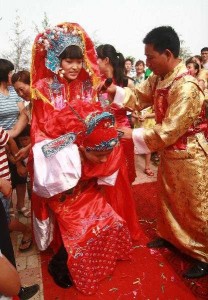 Der chinesische Bräutigam trägt seine Frau auf dem Rücken. Beide in roten traditionellen Gewänder